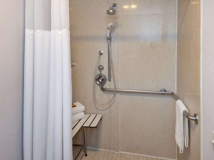 A shower with a handheld showerhead, a handheld shower attachment, and a grab bar.