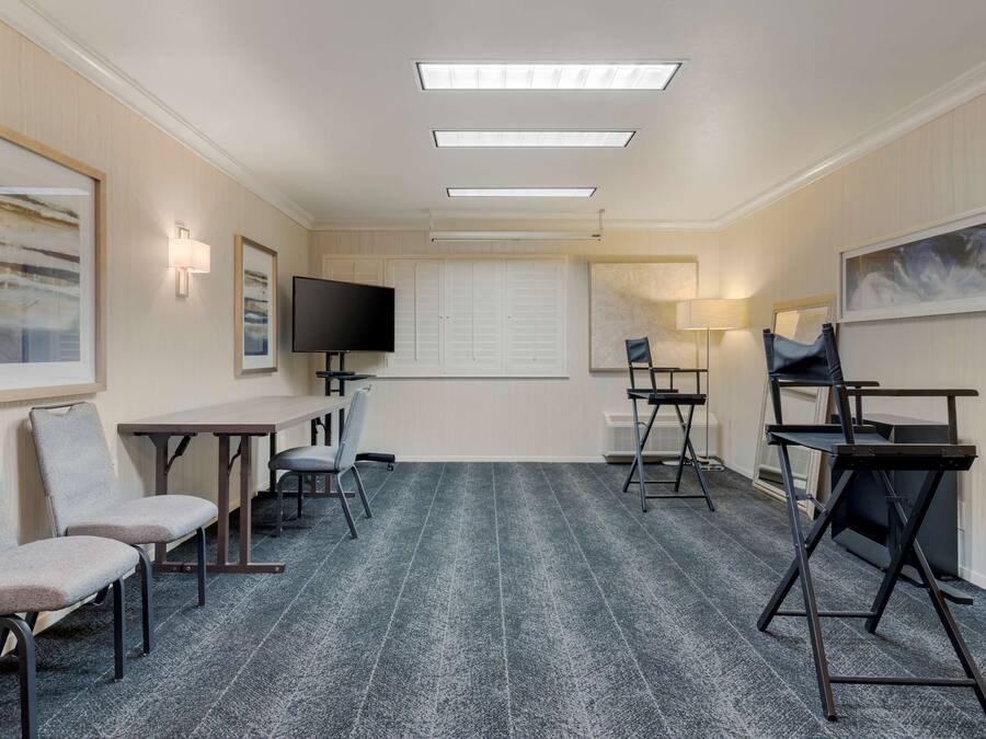 A hotel room with a large bed, a desk, a chair, a TV, and a window with blinds.