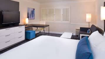 Une chambre d’hôtel équipée d’un lit, d’un bureau, d’une chaise, d’une télévision et d’une fenêtre avec des volets.