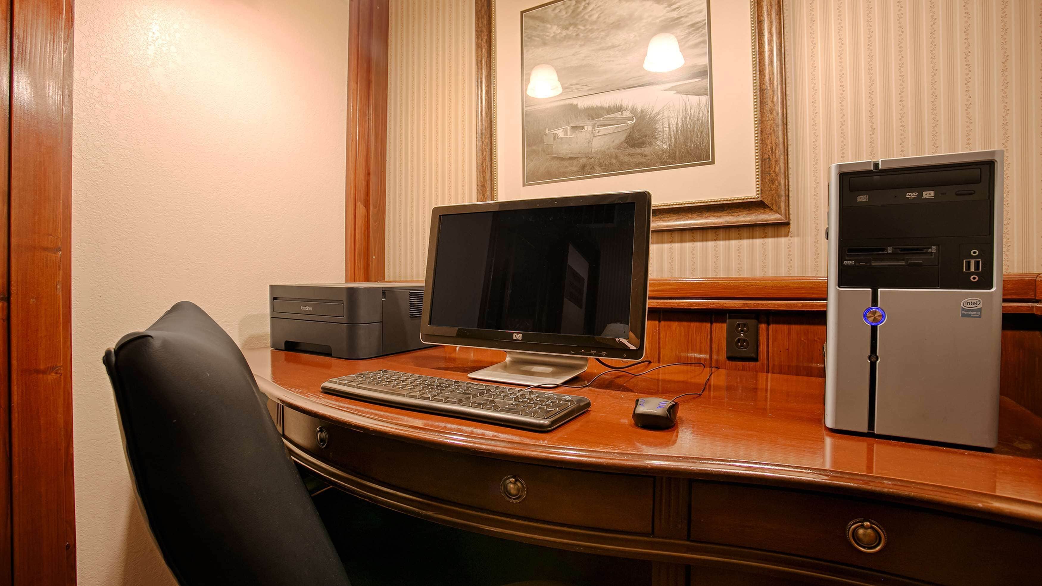 A wooden desk with a desktop computer, a keyboard, and a monitor. There is a chair in front of the desk.