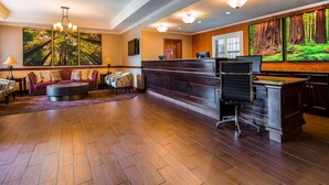 Un hall d’entrée spacieux avec un plancher en bois, un comptoir de réception et un coin salon comprenant un canapé et des fauteuils.