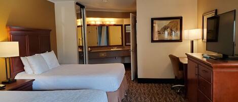 A hotel room with two beds, a desk, a television, and a bathroom visible through an open door.