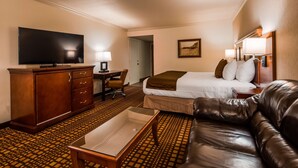 Une chambre d’hôtel avec un lit, un canapé en cuir, un bureau avec une chaise, une télévision et un tableau accroché au mur.