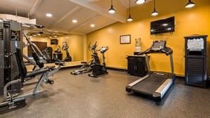Une salle de sport équipée de divers appareils d’exercice, d’un tapis de course et d’un miroir.