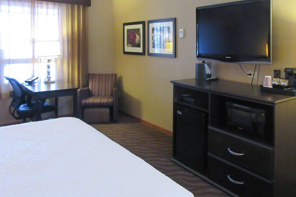 A hotel room with a large bed, a desk with a chair, a television, and a microwave.