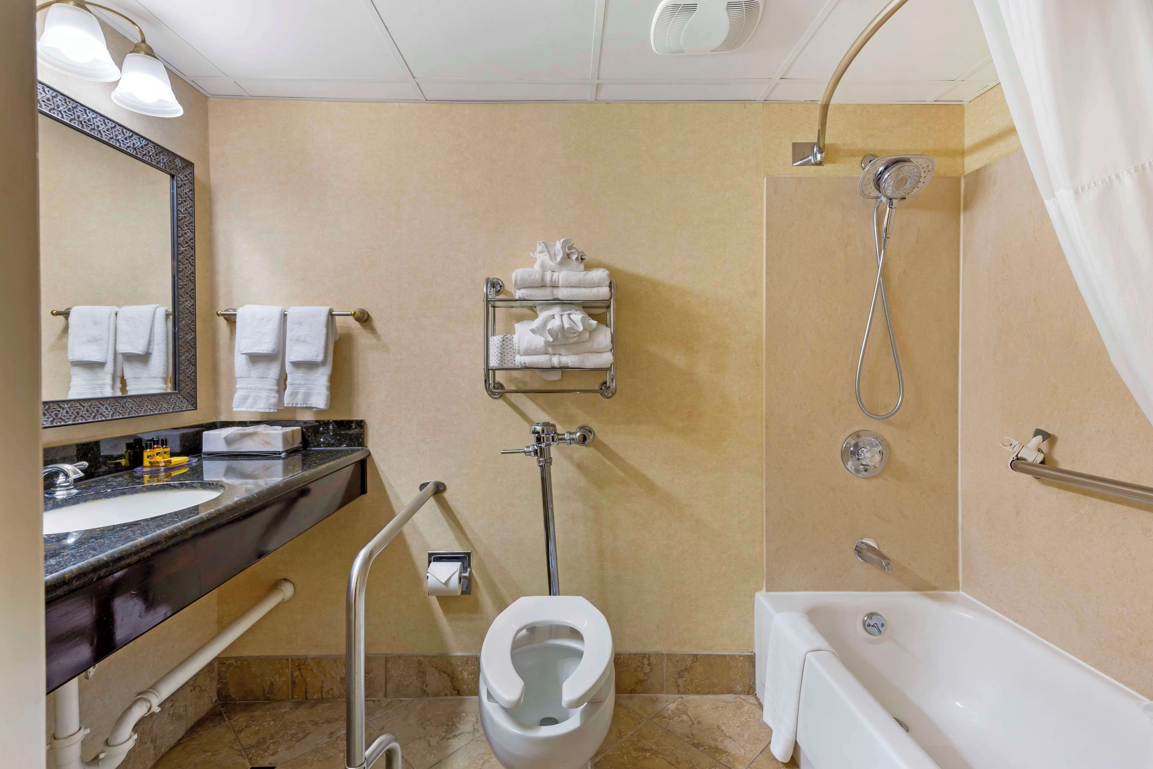 Un baño moderno con lavamanos, inodoro y bañera. Hay toallas en la pared y un cabezal de ducha.