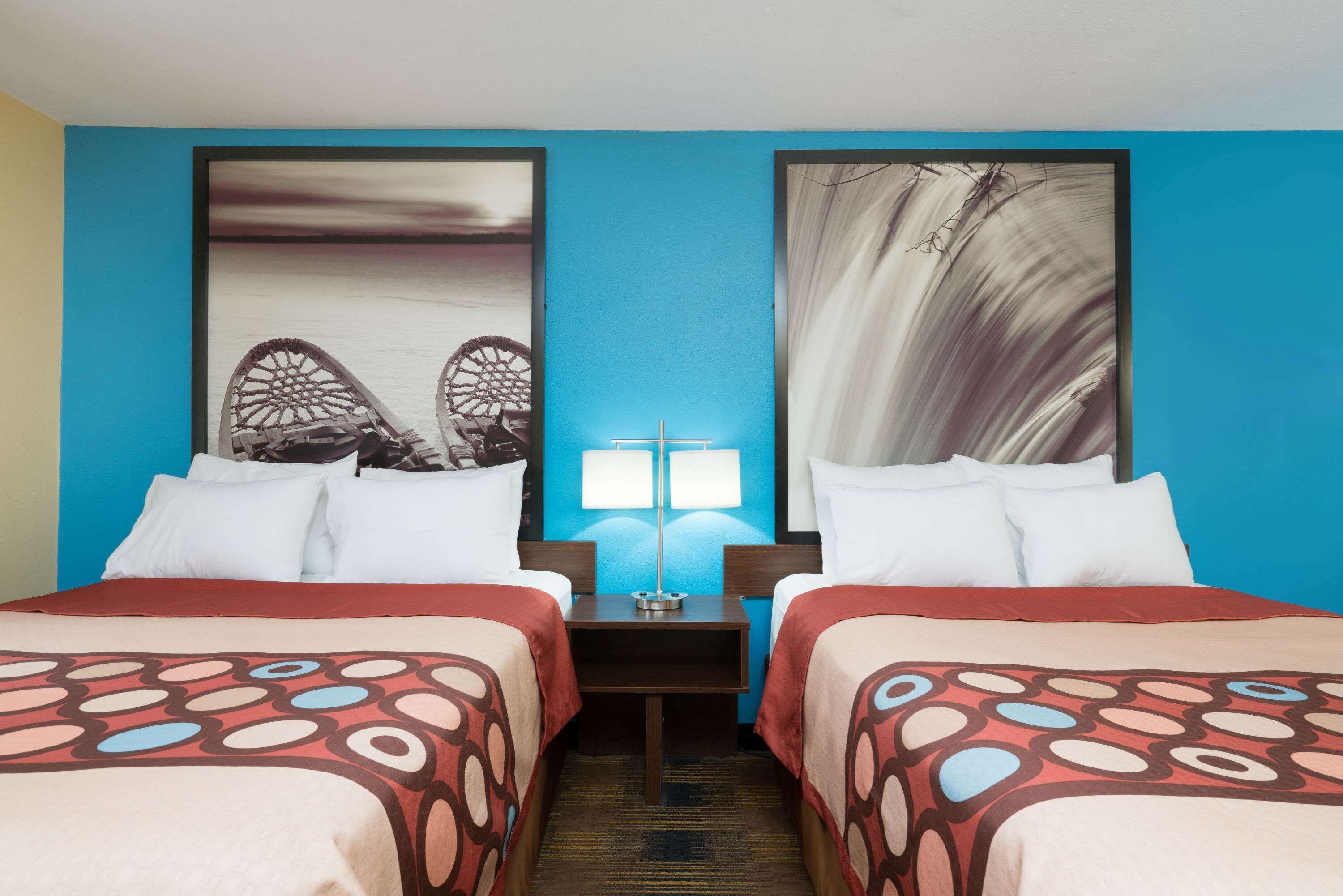 A hotel room with two beds, a nightstand with a lamp, and two framed pictures on the wall.