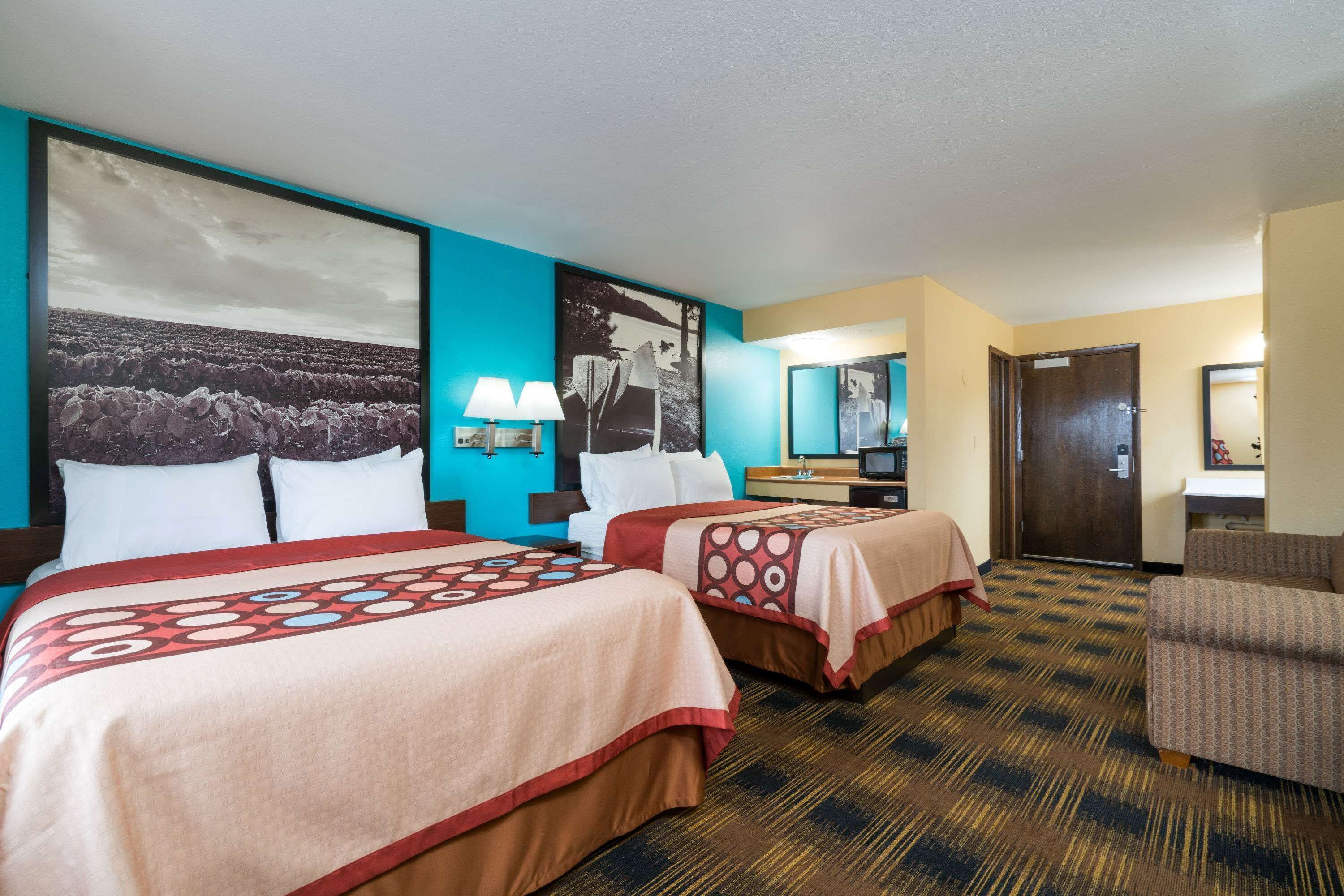 A hotel room with two beds, a desk, a chair, and a large window.