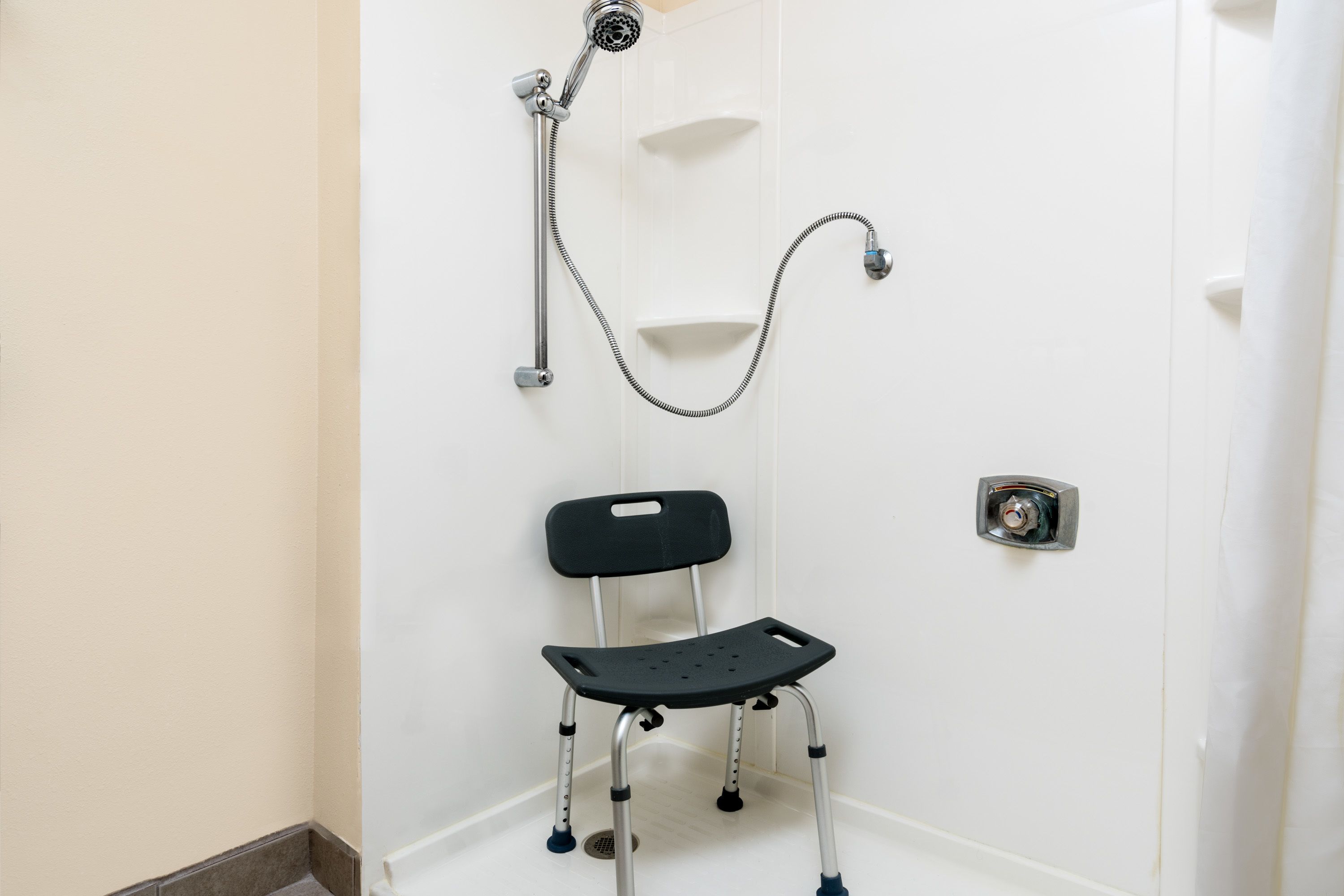 A bathroom with a shower, a black chair with wheels, and a white door.