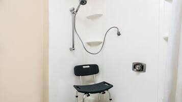 Une salle de bain avec une douche, une chaise noire à roulettes et une porte blanche.
