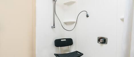 A bathroom with a shower, a black chair with wheels, and a white door.