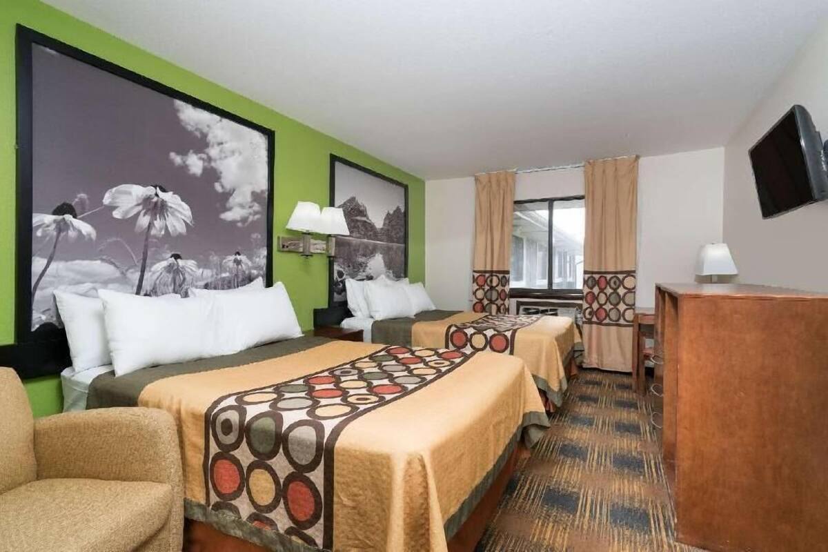 A hotel room with two beds, a desk, a TV, and a large window.