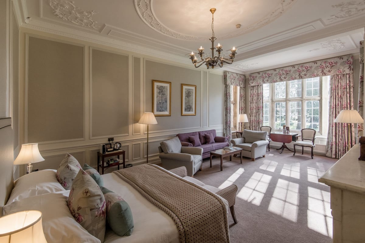 A hotel room with a large bed, two armchairs, a sofa, a small table, and a chandelier.