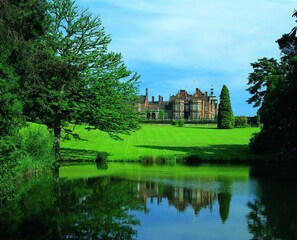 A large, historic building with a symmetrical facade, a central tower, and a well-maintained lawn with a reflecting pond.