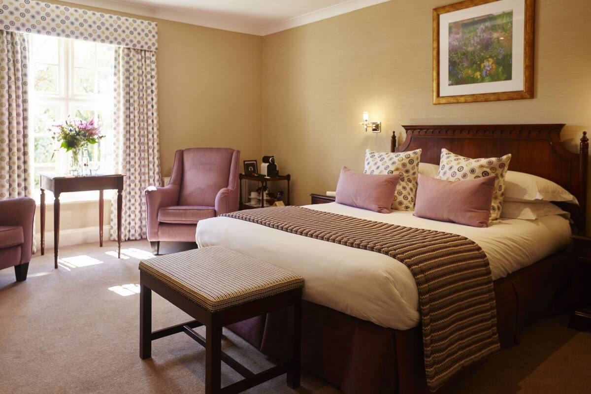 A bedroom with a large bed, a bedside table, a chair, and a window with curtains.