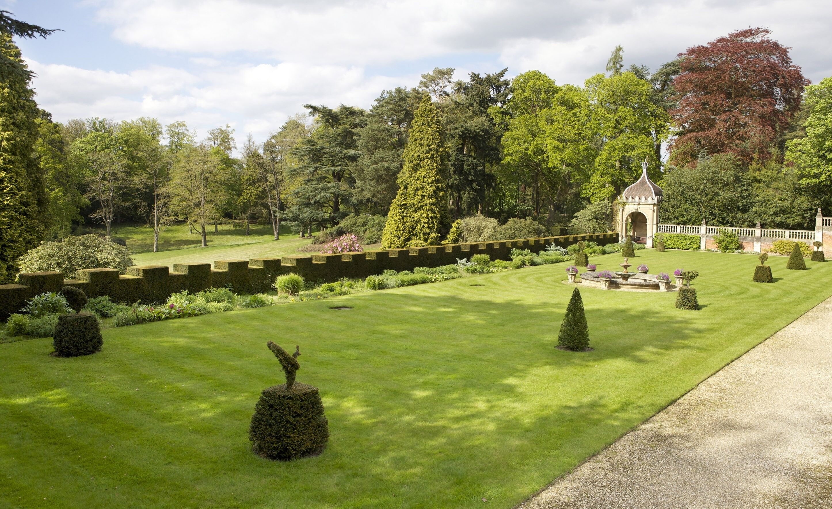 A well-manicured garden with a central lawn, neatly trimmed hedges, and a small gazebo.
