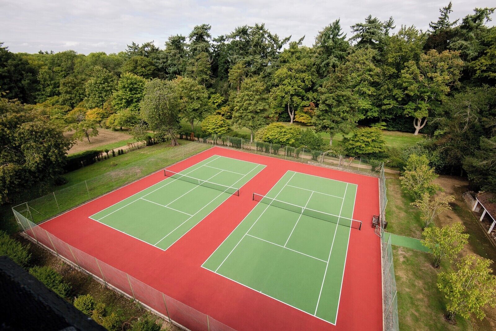 A tennis court with two courts, surrounded by trees and a fence.