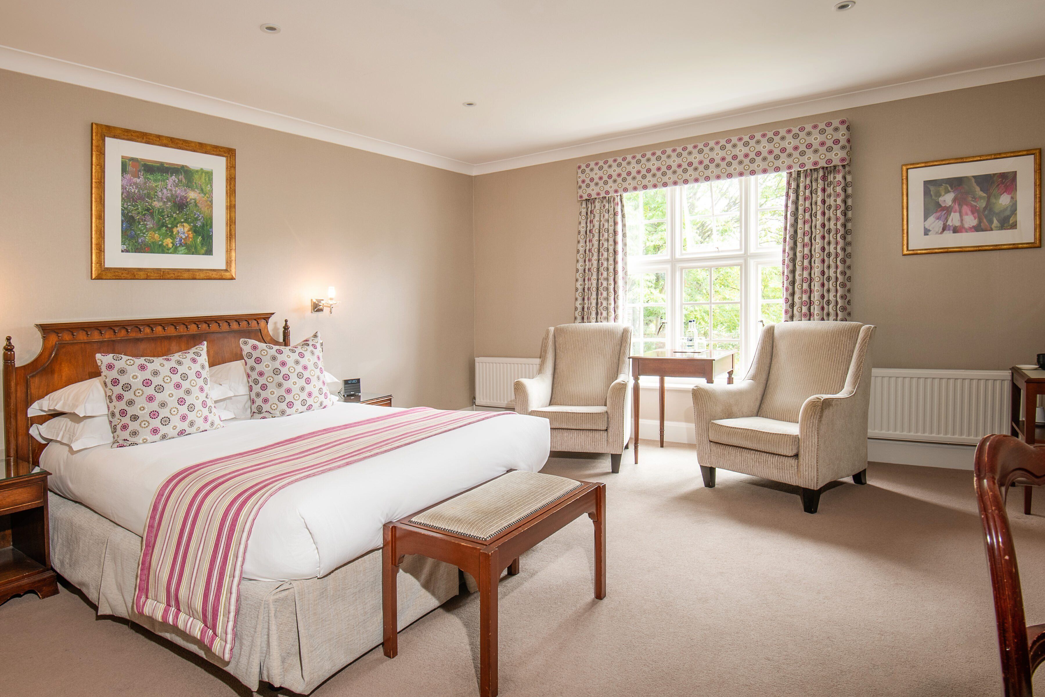 A bedroom with a large bed, two armchairs, a wooden nightstand, and a small table.