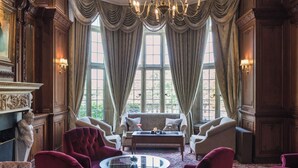Une chambre luxueuse, ornée d’un magnifique lustre, de meubles élégants et de grandes fenêtres surmontées de rideaux.