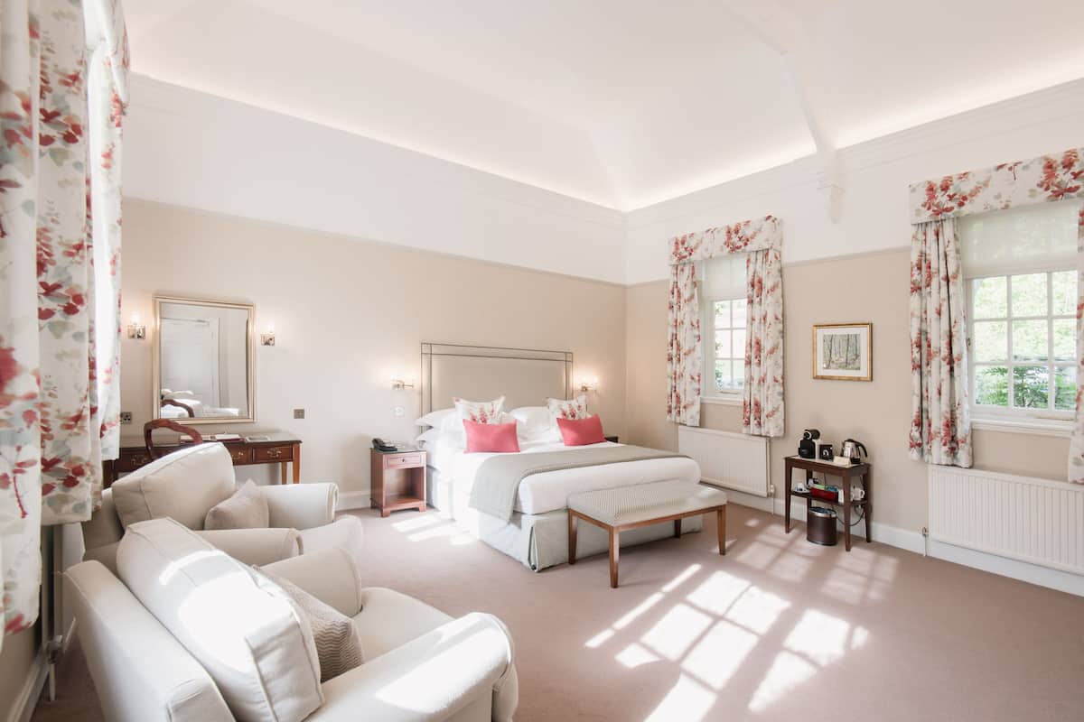 A spacious bedroom with a large bed, a sitting area with a bench, and a view of the outdoors through the window.