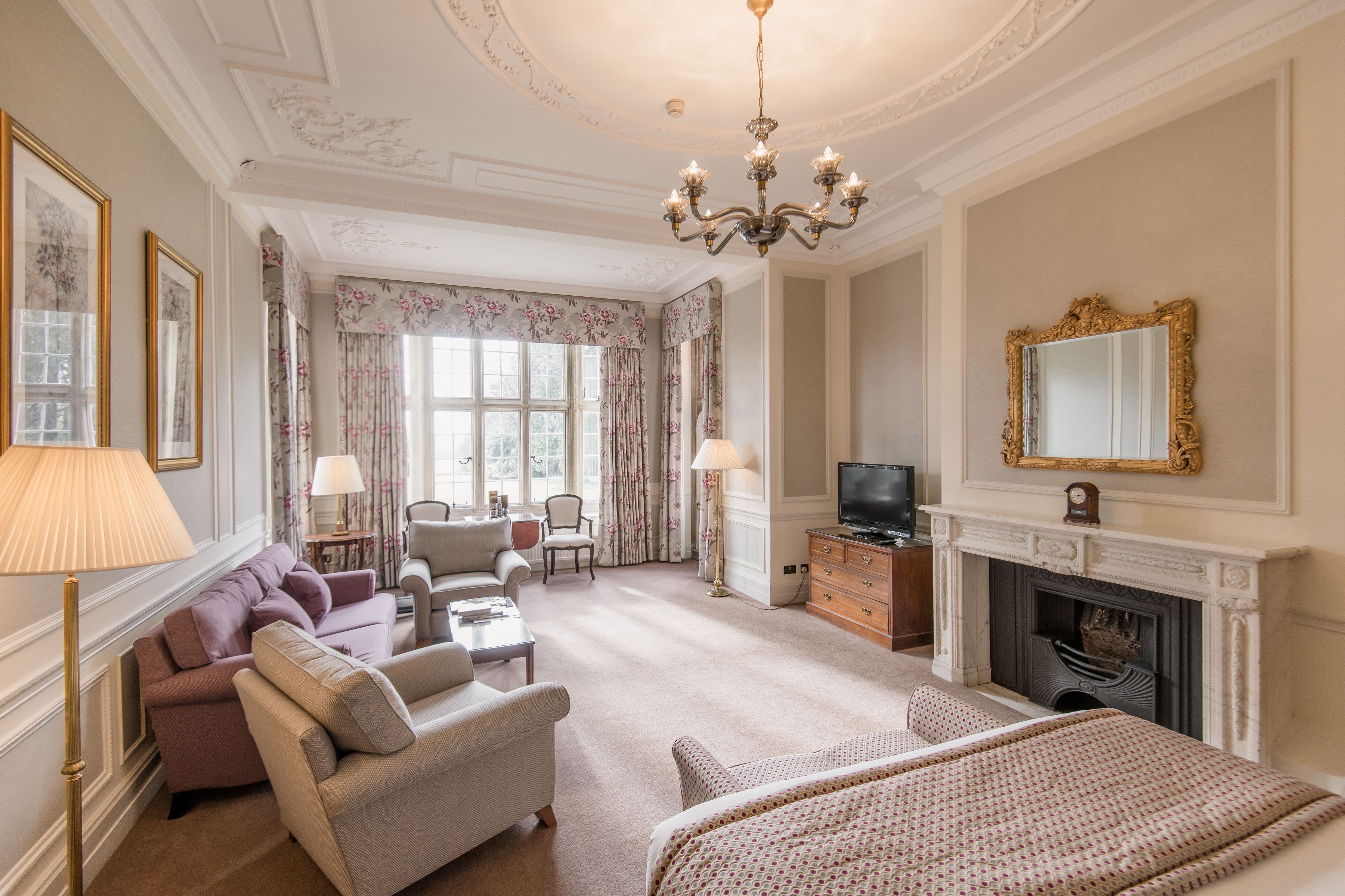 Une chambre d’hôtel spacieuse, dotée d’un grand lit, d’un coin salon avec un canapé et des fauteuils, d’une cheminée et d’une télévision.