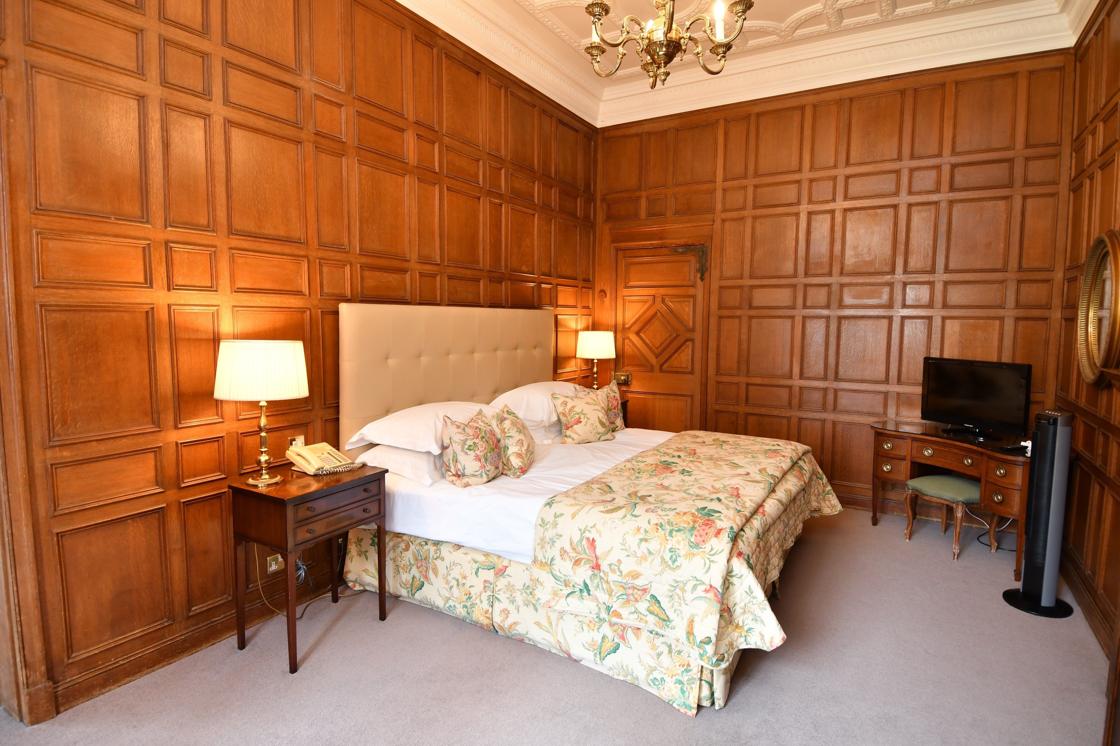 Ein Hotelzimmer mit einem großen Bett, Holzwandverkleidung, einem Schreibtisch mit Fernseher und einem Sessel.