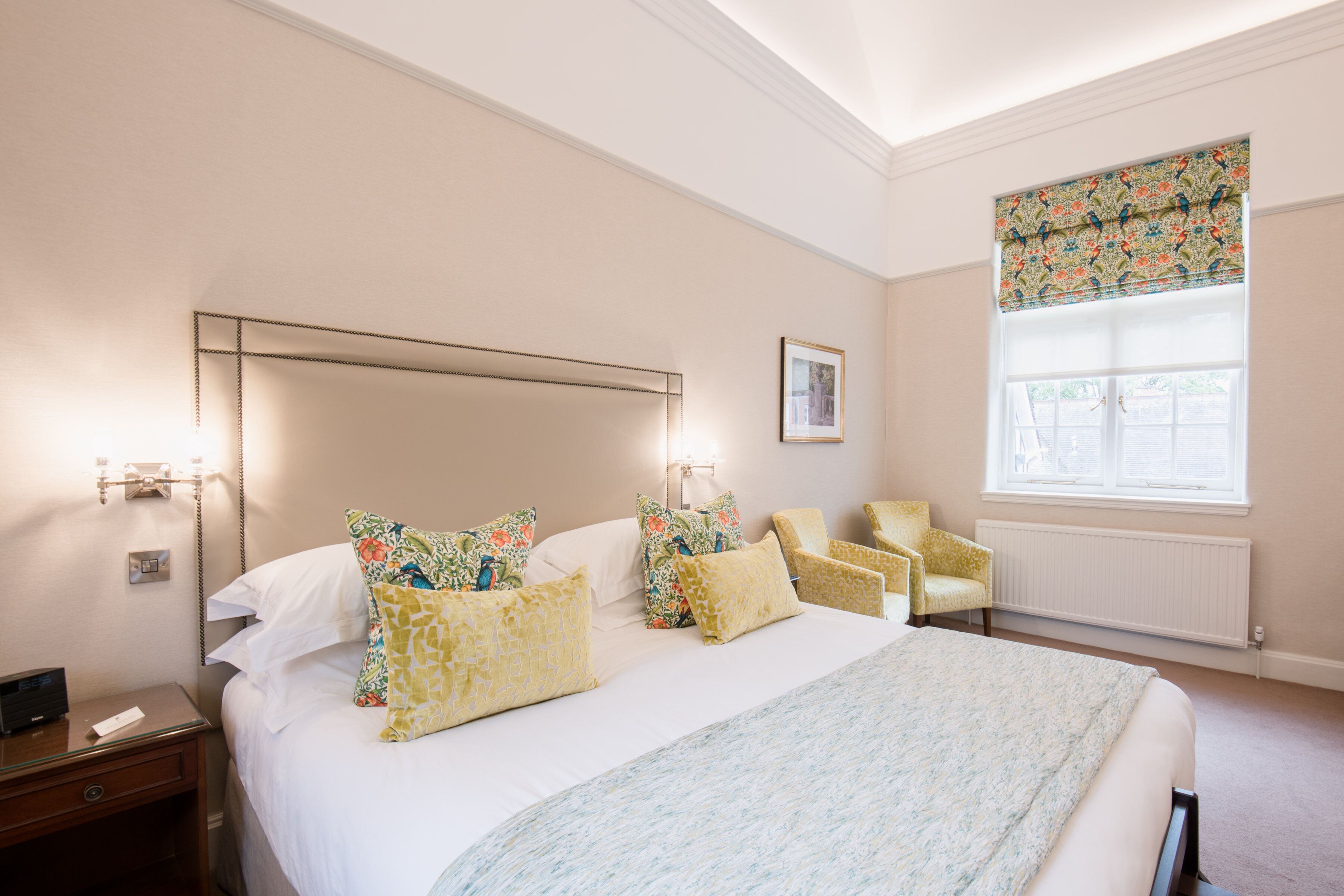 A hotel room with a large bed, a chair, a nightstand, and a window with a patterned blind.