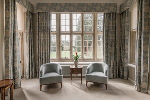 A room with two armchairs, a small table with a vase, and a large window with curtains.