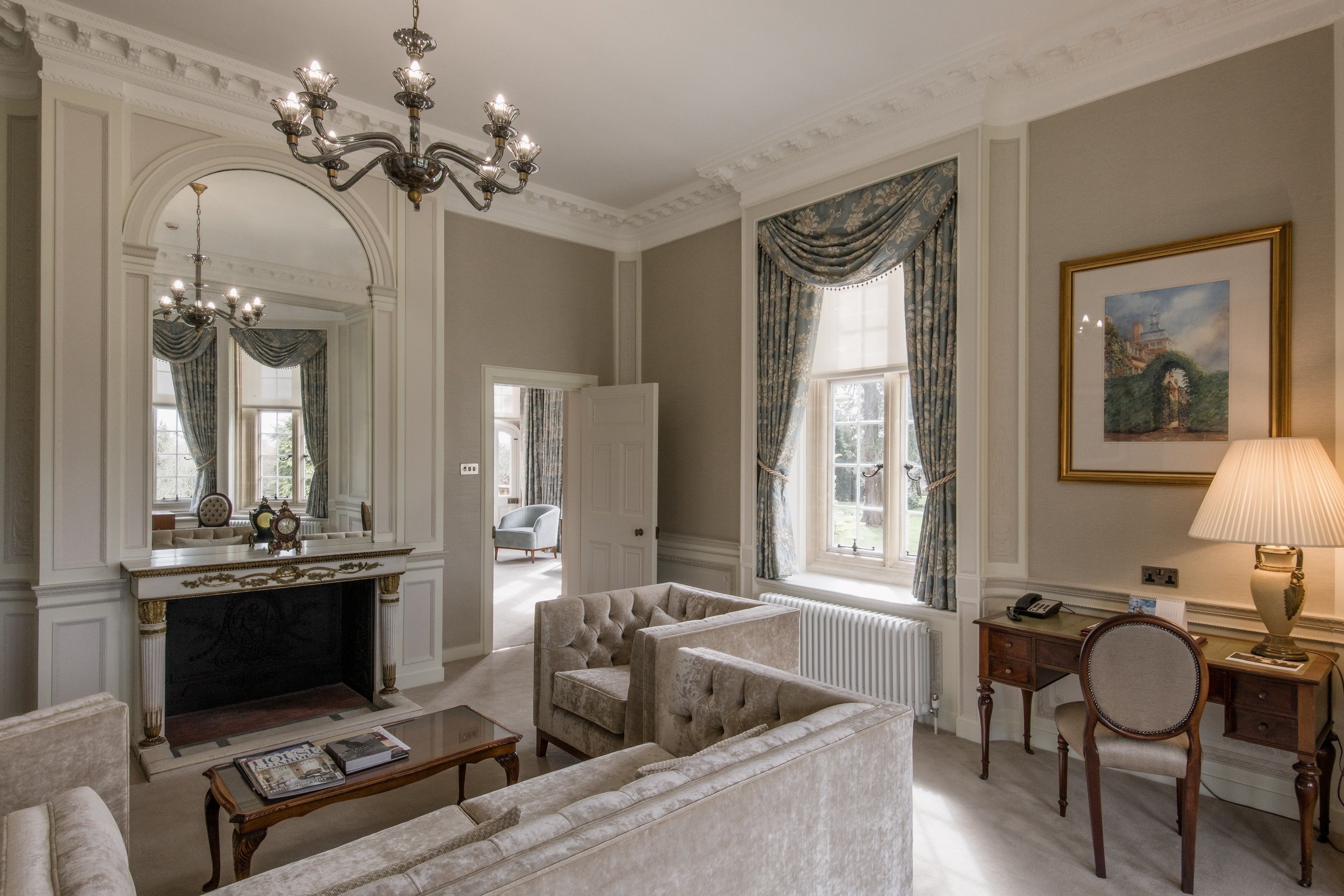 A spacious living room with a fireplace, elegant furniture, and a chandelier.