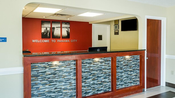 A reception desk with a red wall, a laptop, and a glass panel design. - Rodeway Inn Panama City (Panama City)