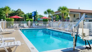 A swimming pool with white lounge chairs and a red umbrella, surrounded by a white fence and palm trees. - Rodeway Inn Panama City (Panama City)