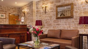 A lobby with stone walls, a wooden reception desk, a brown leather sofa, and a glass coffee table with magazines.