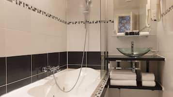 Une salle de bain moderne avec une baignoire entourée de parois en verre, un mur recouvert de carreaux noirs et blancs, un lavabo en verre et un miroir au-dessus du lavabo.