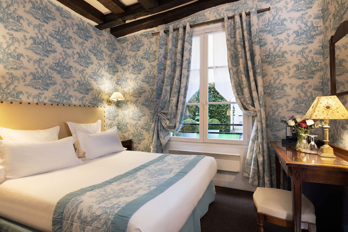 A bedroom with a large bed, a desk with a lamp, and a window with curtains.