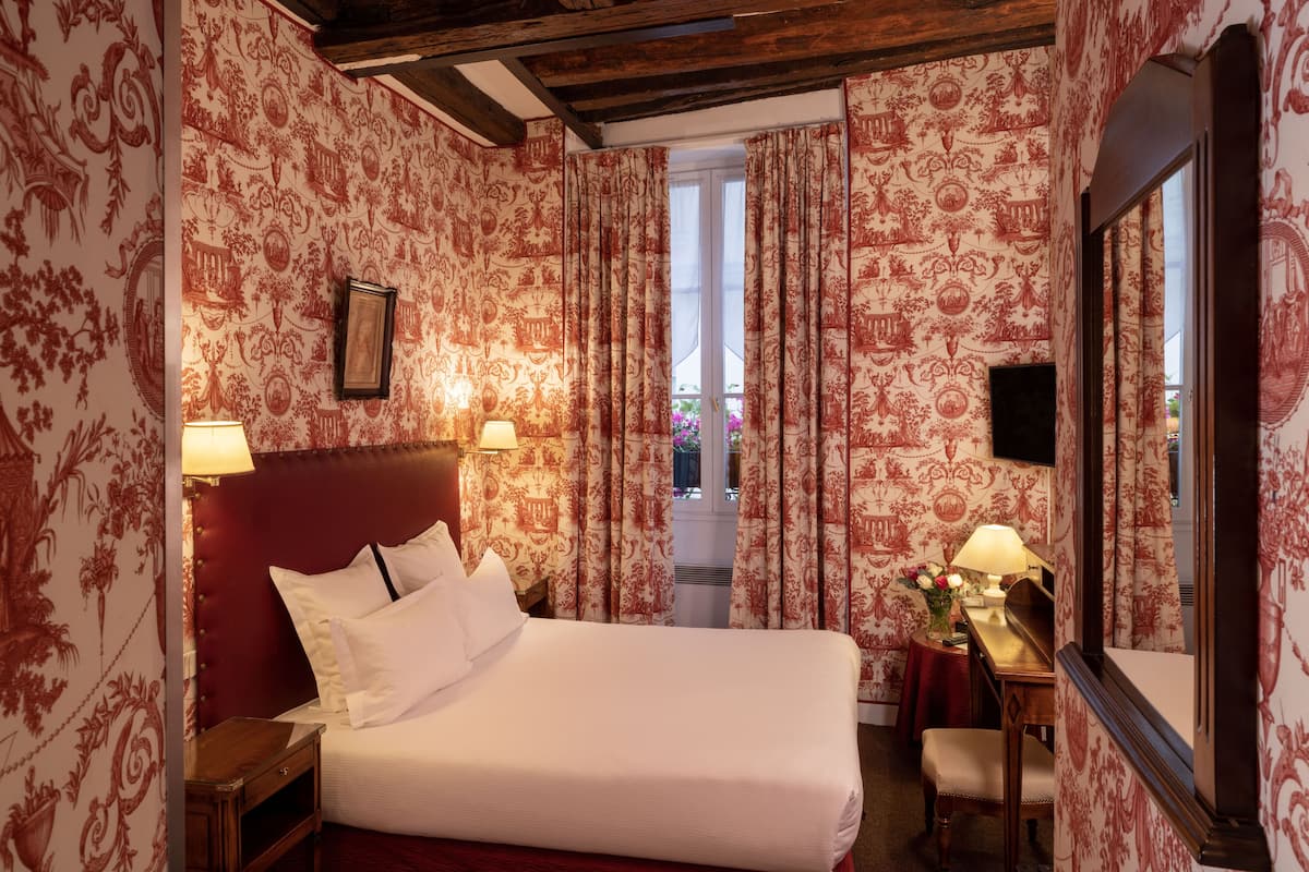 A hotel room with a large bed, two bedside tables with lamps, a desk with a chair, and a large mirror.