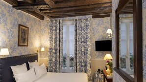 A hotel room with a bed, two bedside lamps, a nightstand, a desk with a lamp, a framed picture, and a window with curtains.