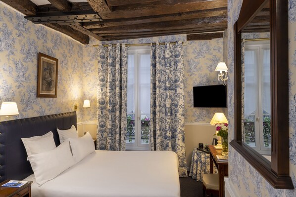 Una habitación de hotel con una cama, dos lámparas de noche, una mesita de noche, un escritorio con lámpara, un cuadro enmarco y una ventana con cortinas.
