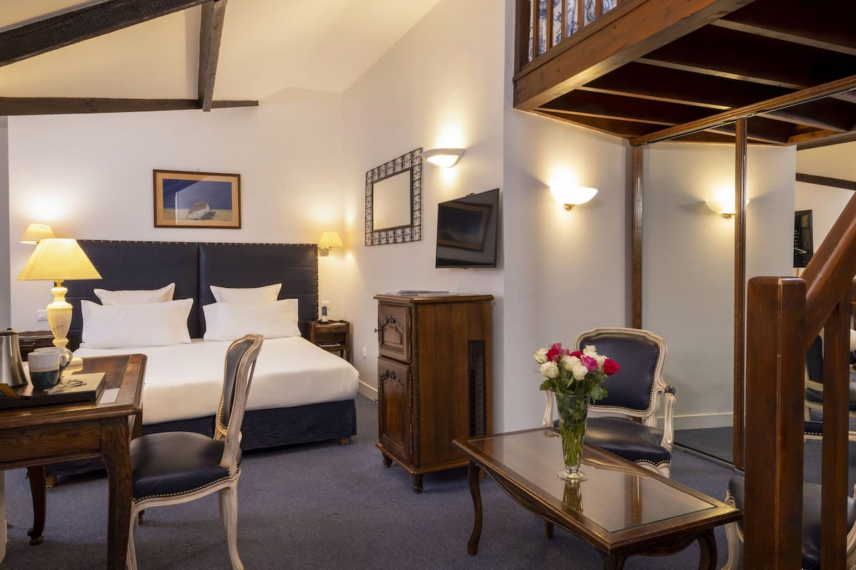 A hotel room with a large bed, a desk with a lamp, a chair, a dresser, and a vase with flowers.