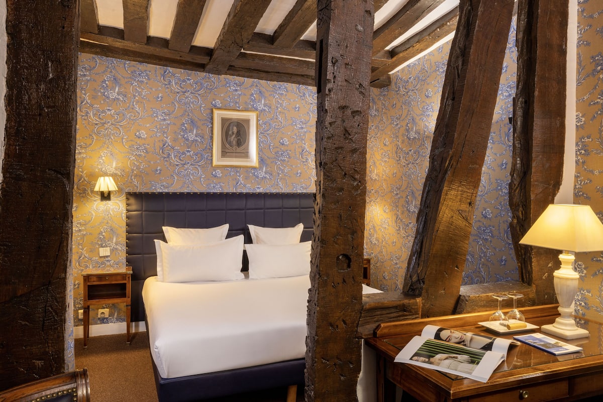 A hotel room with a large bed, wooden beams, and a patterned wallpaper.