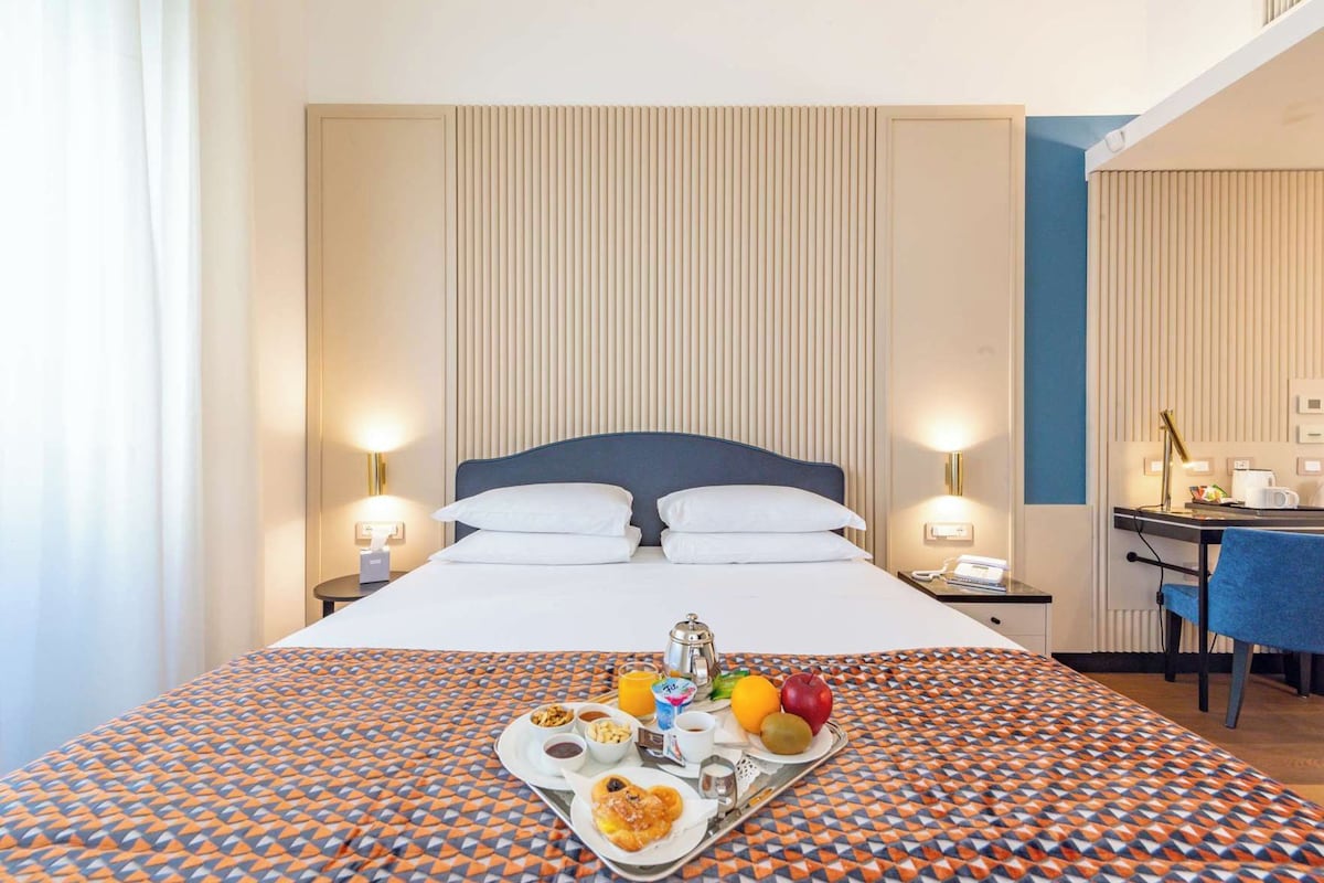 A hotel room with a bed, bedside tables, a desk, and a tray with breakfast.