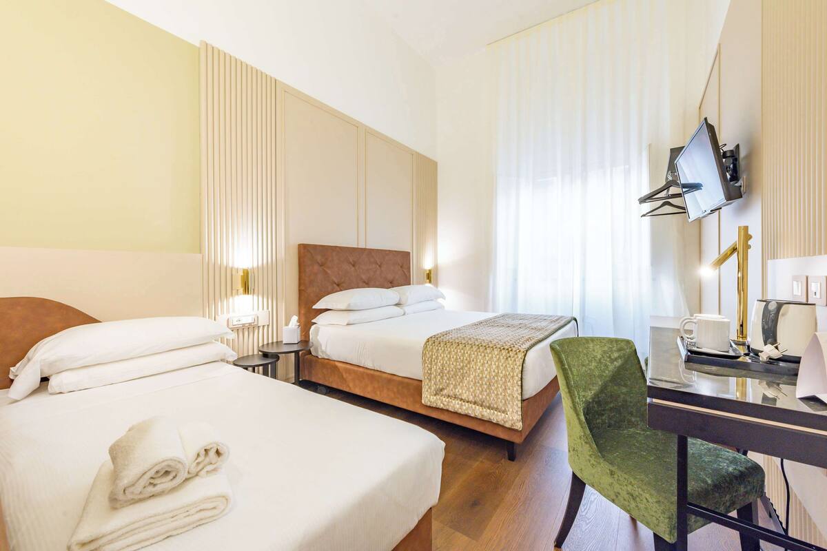 Une chambre d’hôtel avec deux lits, un bureau avec une chaise, une télévision et une fenêtre avec des rideaux.