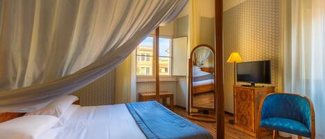 A hotel room with a bed, a TV, a chair, and a window with curtains.