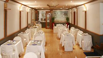 Un salón de banquetes con mesas dispuestas para un evento formal, que incluye un bufé central y un cuadro grande en la pared de fondo.