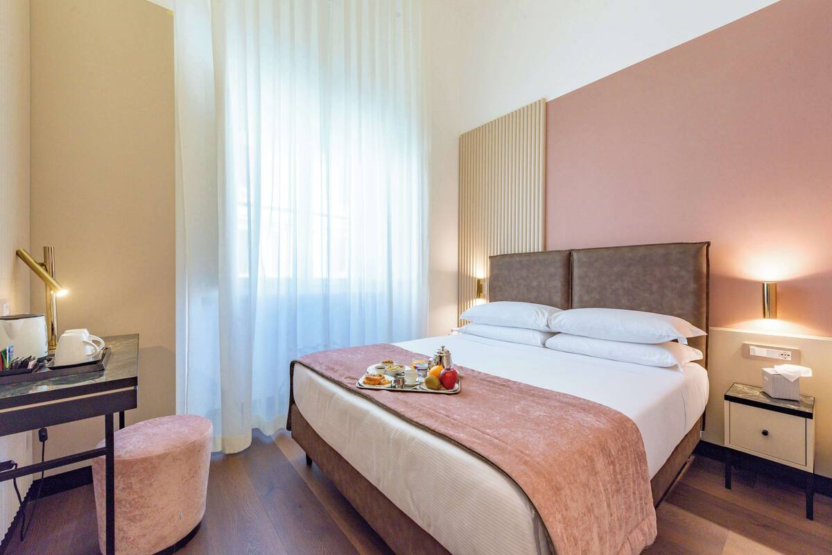A hotel room with a bed, bedside table, desk, and a window with curtains.