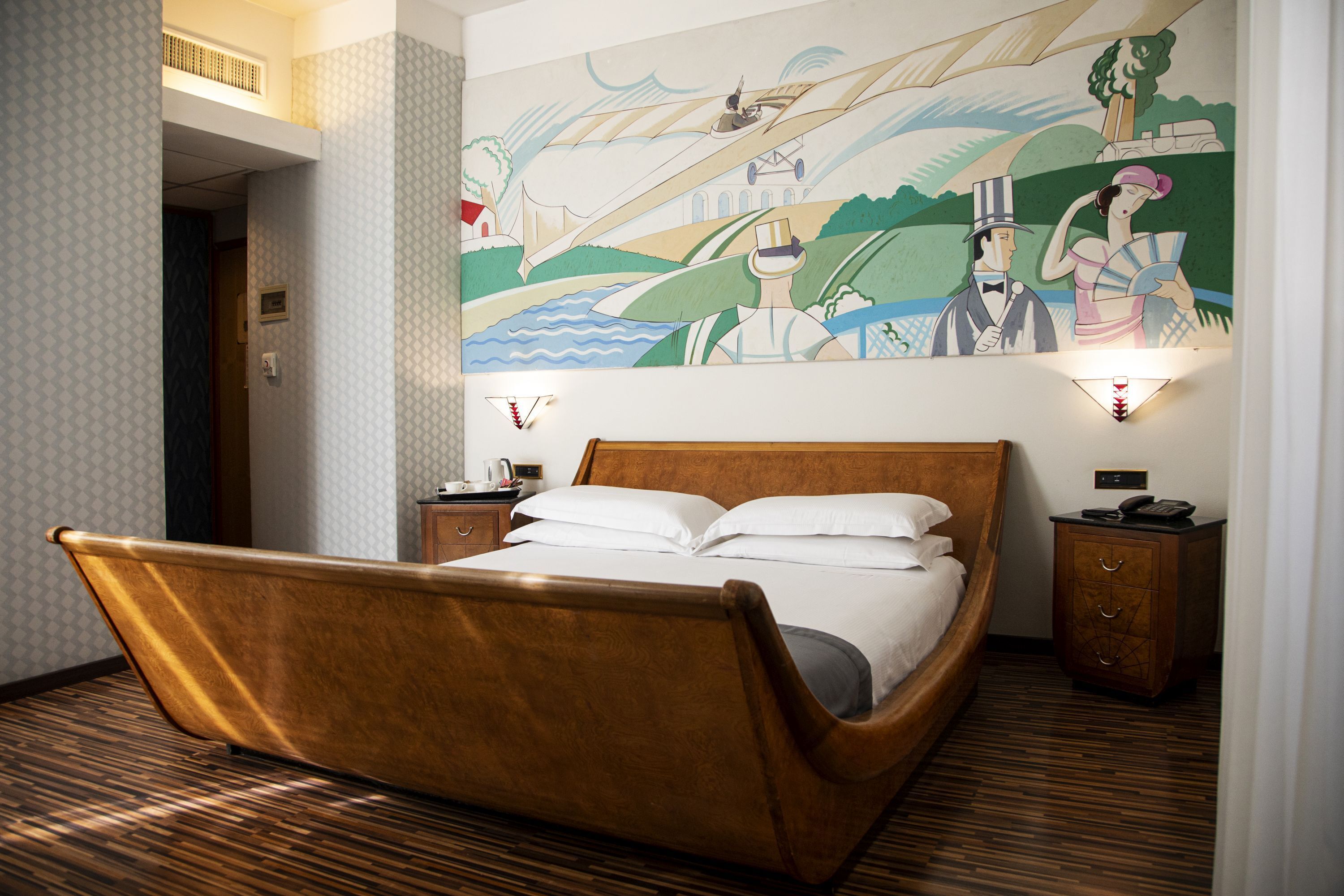 Una habitación con una cama de madera, un mural en la pared y una mesita de noche con una lámpara.