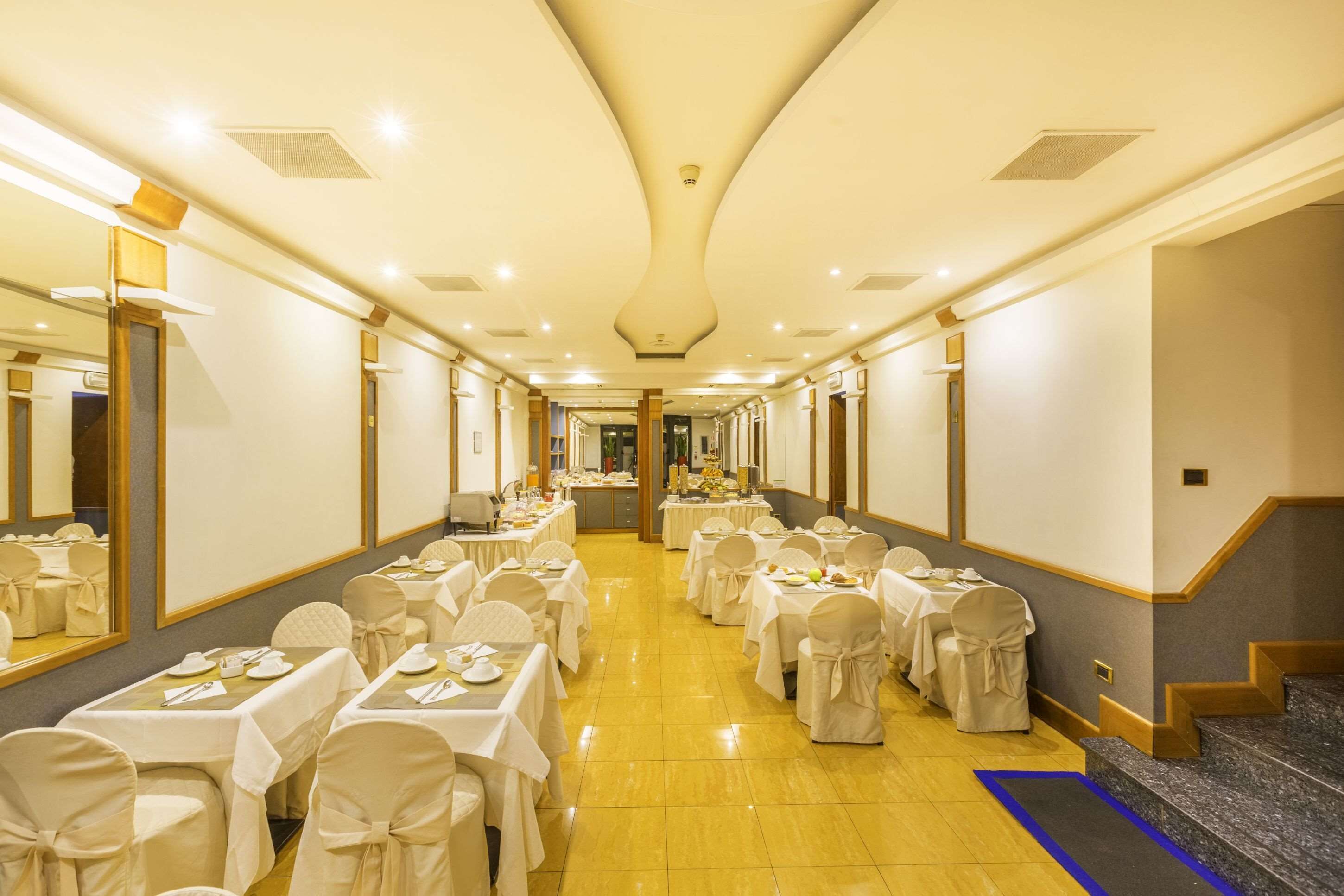Un salón de banquetes con mesas dispuestas para un evento formal, que incluye un largo pasillo y una escalera.