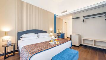 Una camera d'albergo con un letto grande, un comodino con una lampada, una scrivania con una sedia e un armadio.