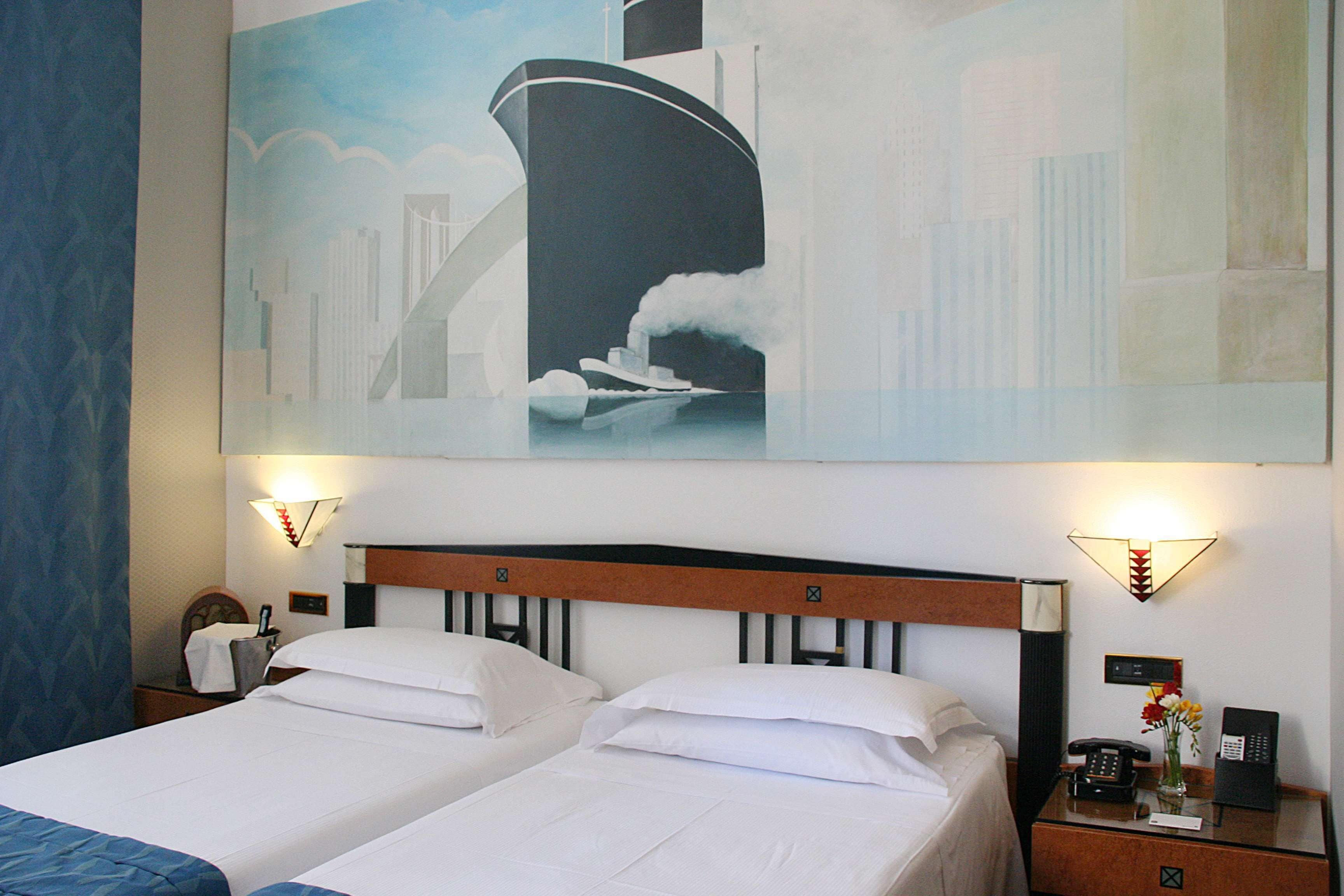 A hotel room with two beds, a large painting of a ship on the wall, and two bedside lamps.