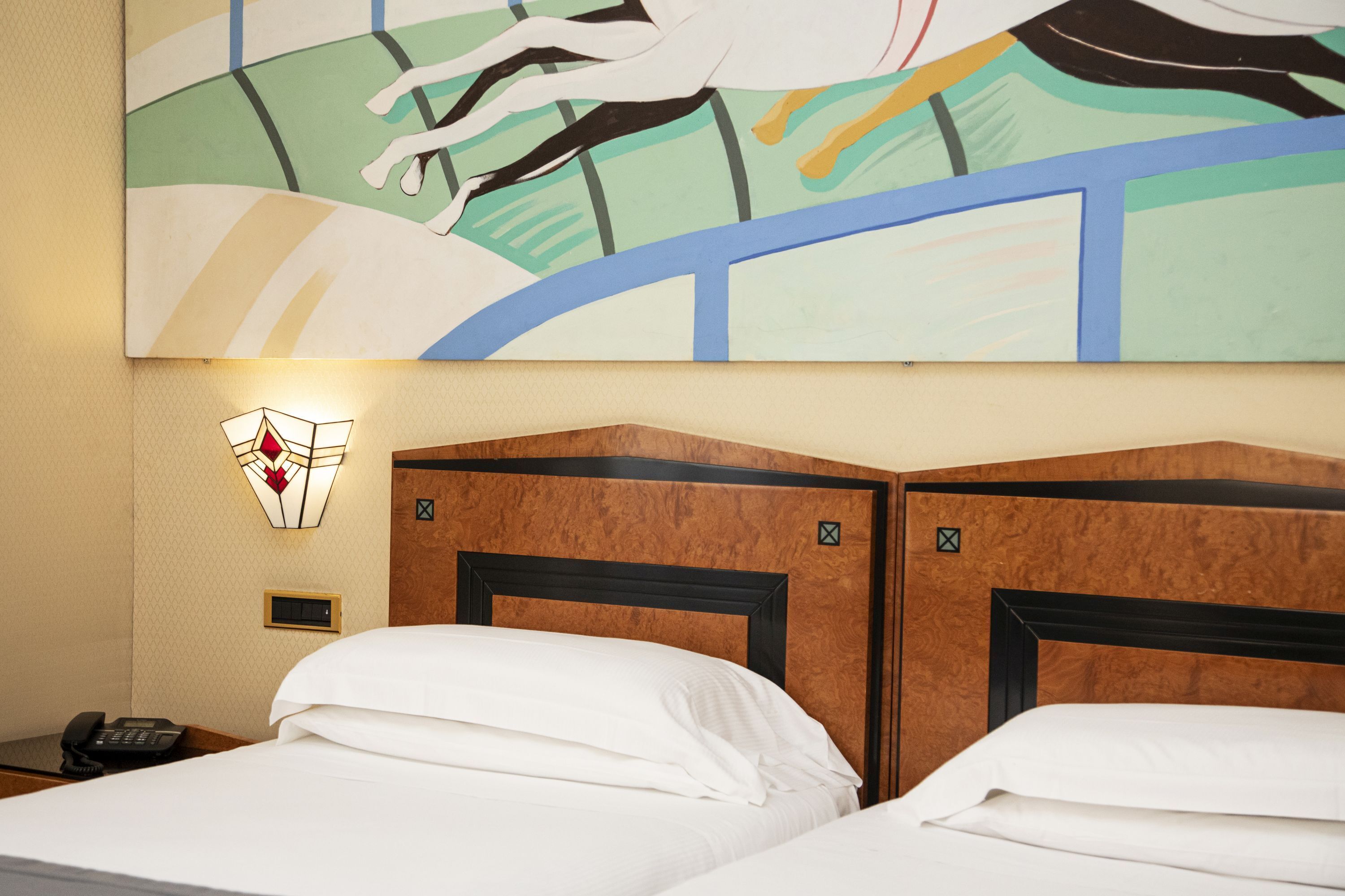 A hotel room with two beds, a wall-mounted phone, and a painting above the beds.