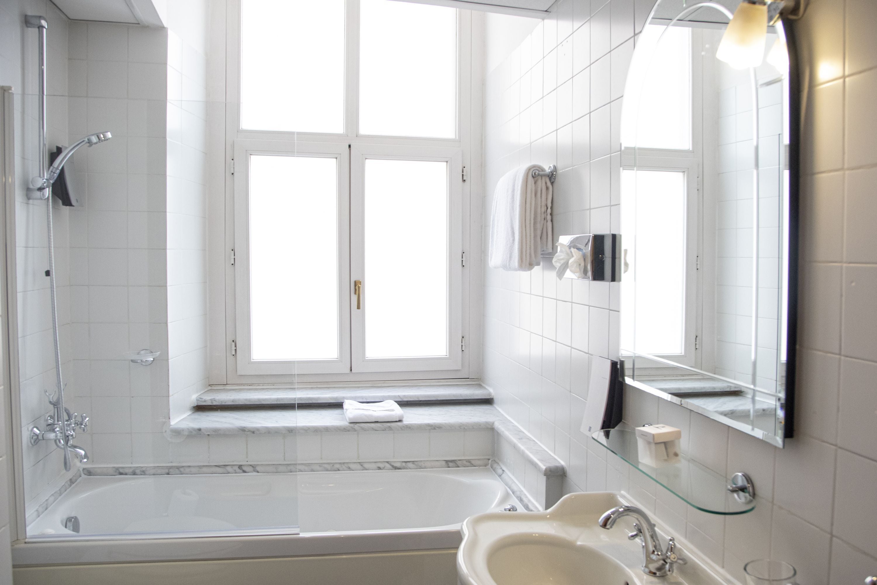 Un bagno moderno con una vasca, un lavandino, uno scaffale in vetro e un'ampia finestra.